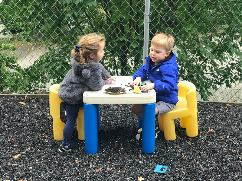 two young children sitting at a small outdoor table