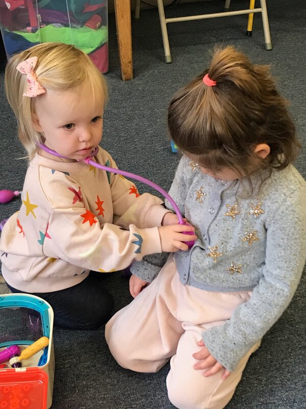 young girl pretending to be a doctor with her friend at preschool